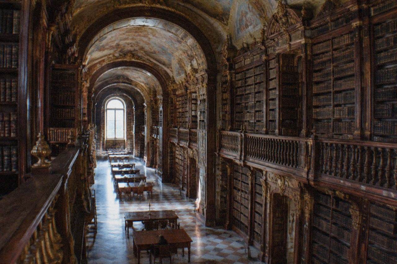 The ornate baroque interior of the Joanina Library in Coimbra with tall wooden bookshelves and a painted ceiling