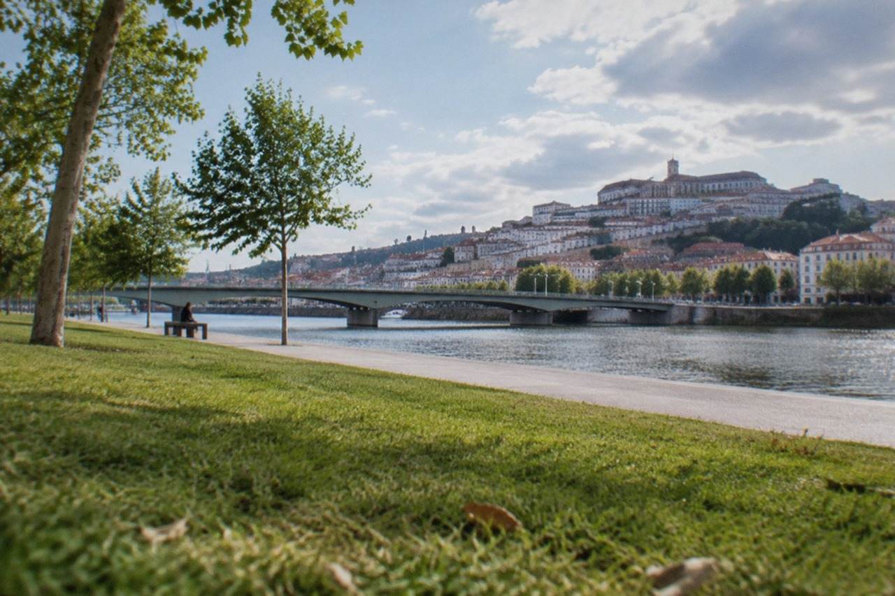 Riverside park lawns beside the River Mondego with the city skyline and university hill behind