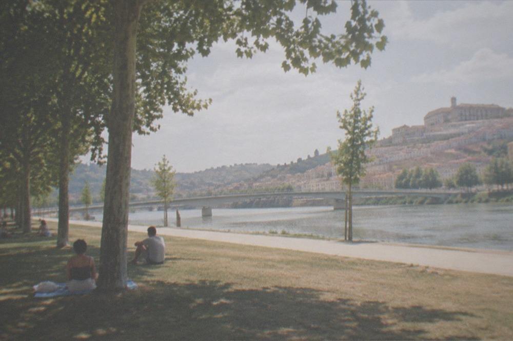 Summer afternoon on the riverbank lawns with people sitting in the shade of riverside trees