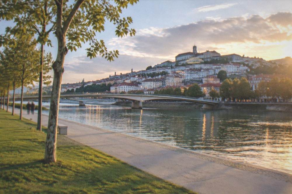 Evening view along the illuminated riverfront path with the old town lights reflected in the Mondego