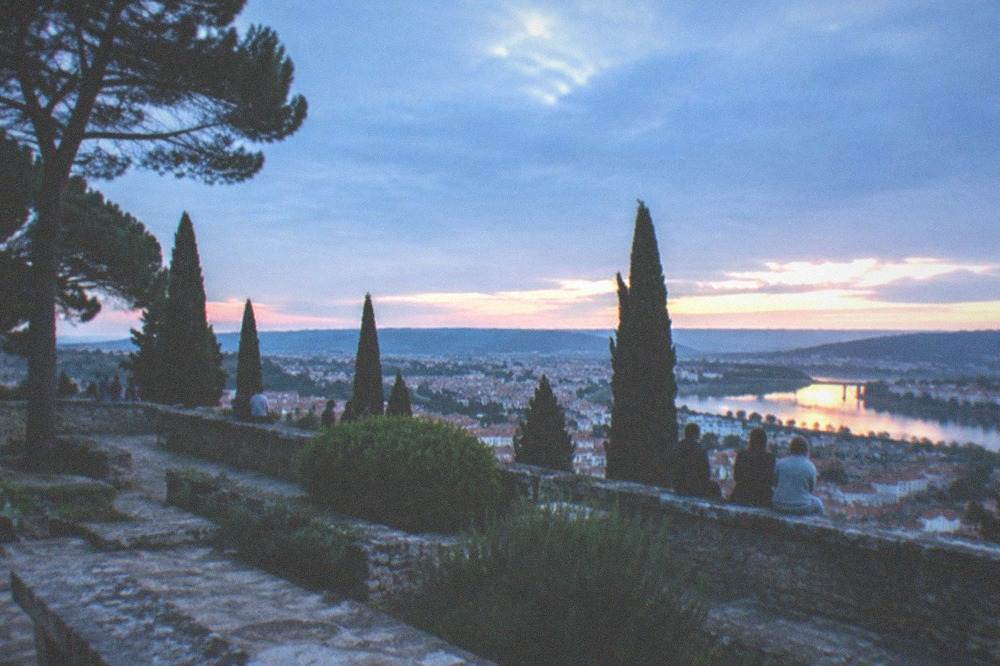 Visitors sitting on a stone balustrade watching the sunset light on the far riverbank