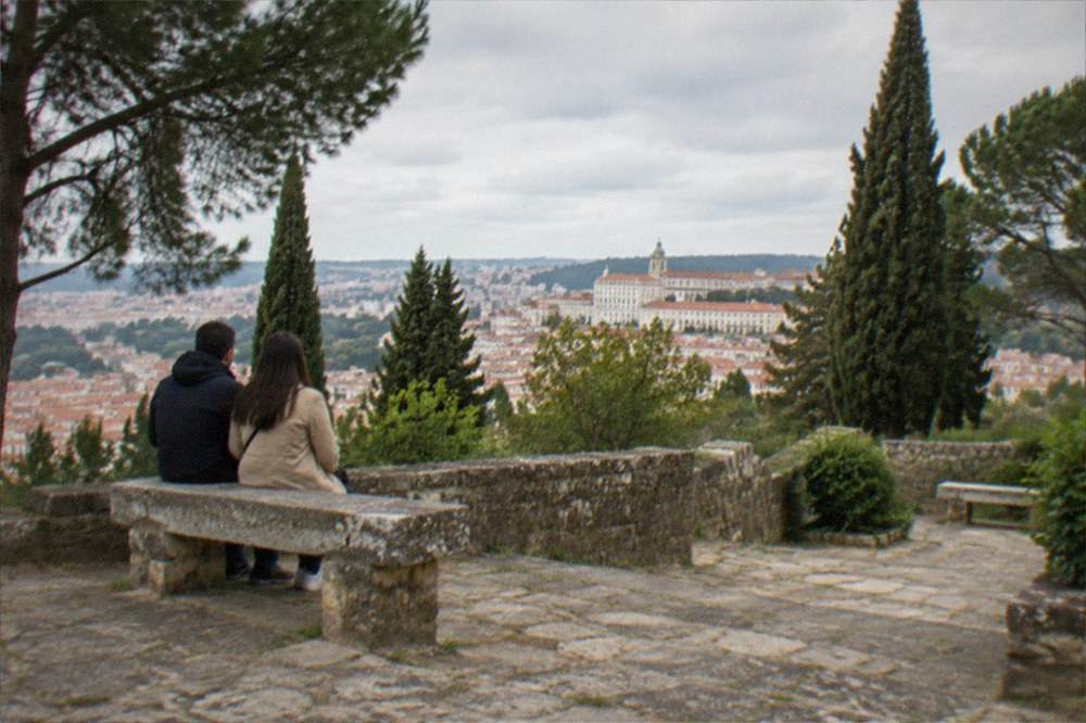 A couple pausing at a stone bench on a garden terrace above the city