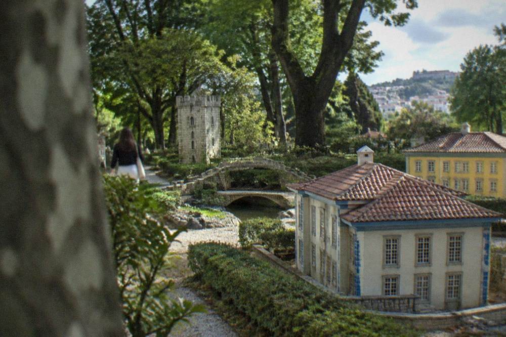 A miniature stone tower and small bridge among trees inside the park
