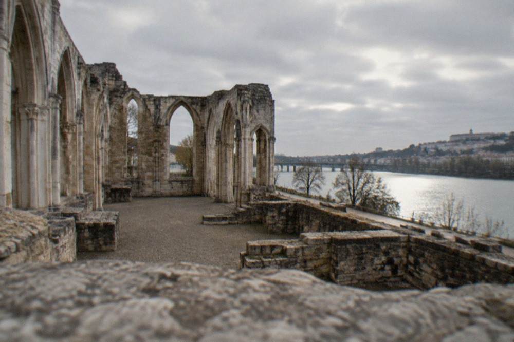 Excavated stone walls of a medieval church rising from ground level, with a river visible beyond
