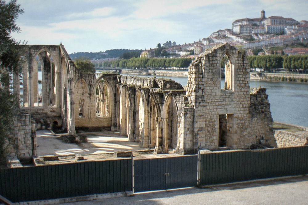 Closed gate and hoarding in front of an old stone monument, with no visitors present
