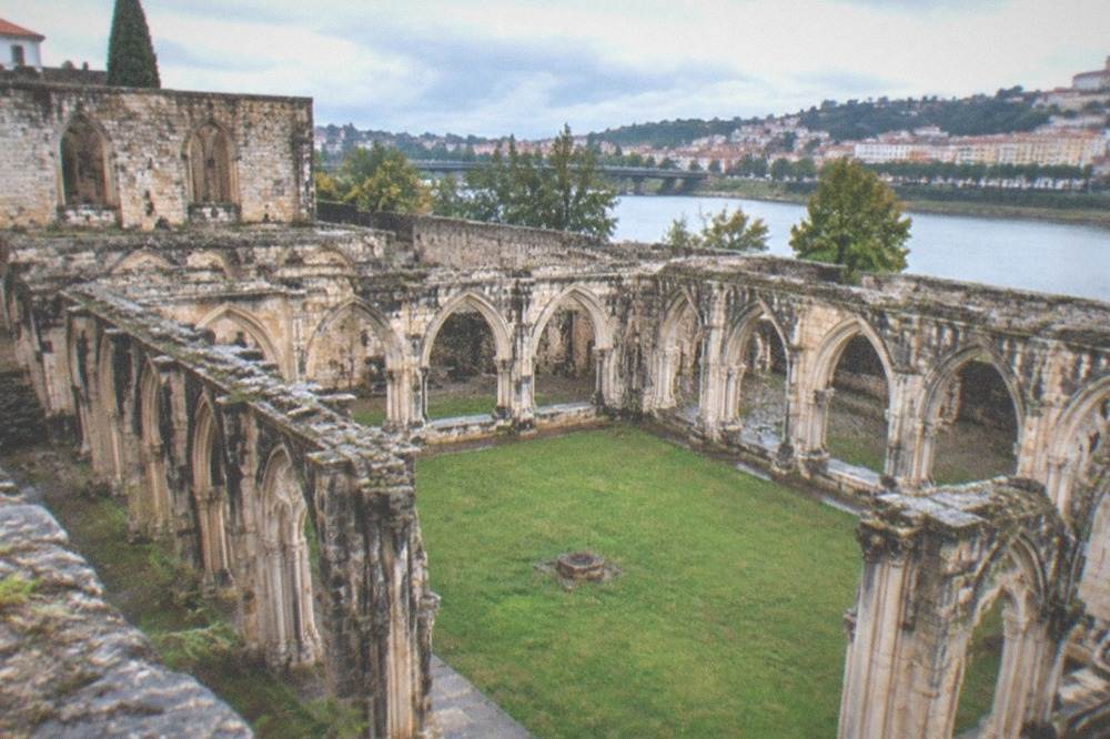 Interior of an excavated stone cloister with arched walkways and a grassed central court