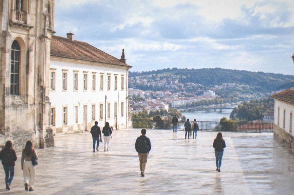 Sunlit university courtyard with students walking between historic stone buildings in Coimbra