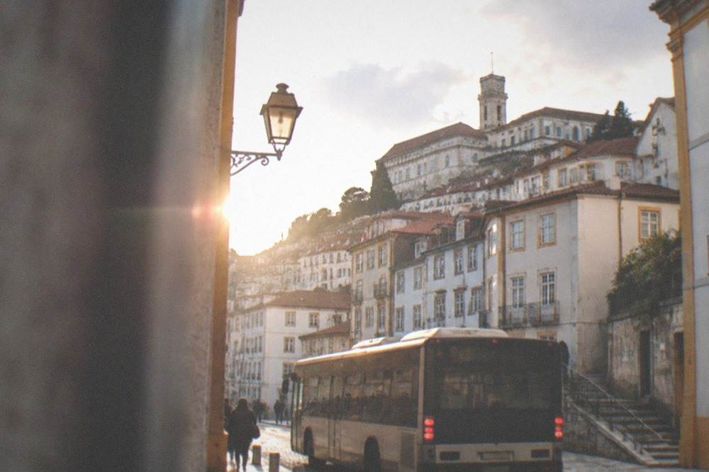 A city bus on a street in central Coimbra with old buildings behind