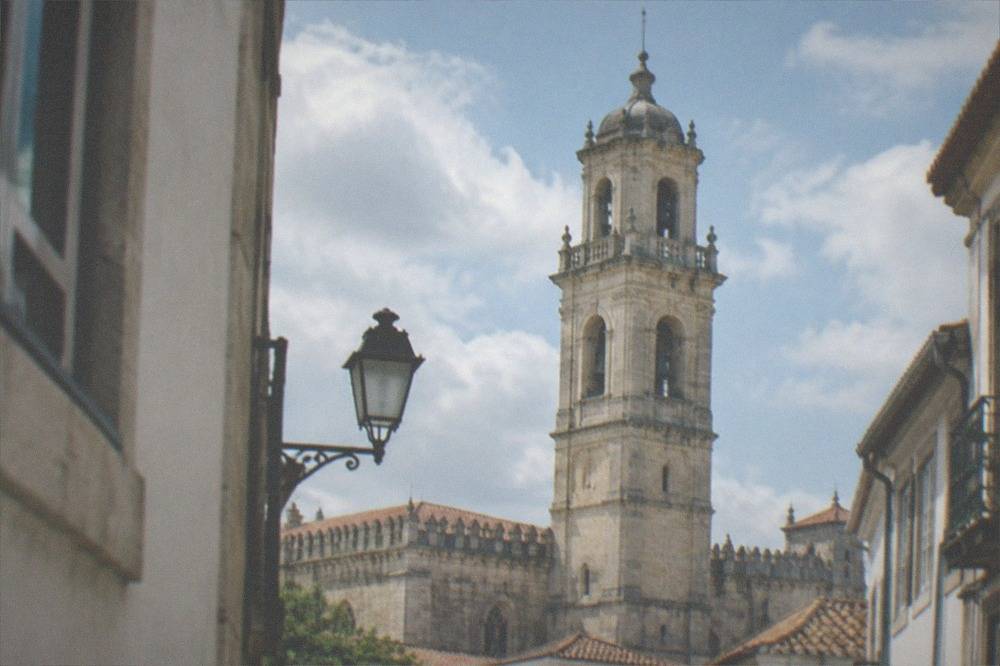 The bell tower and crenellated roofline of the old cathedral seen against the sky from a narrow street in Coimbra