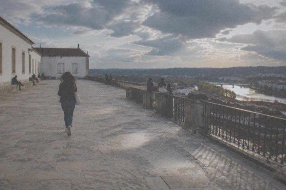Visitors resting on the wall of the Paço das Escolas with the River Mondego and city rooftops below
