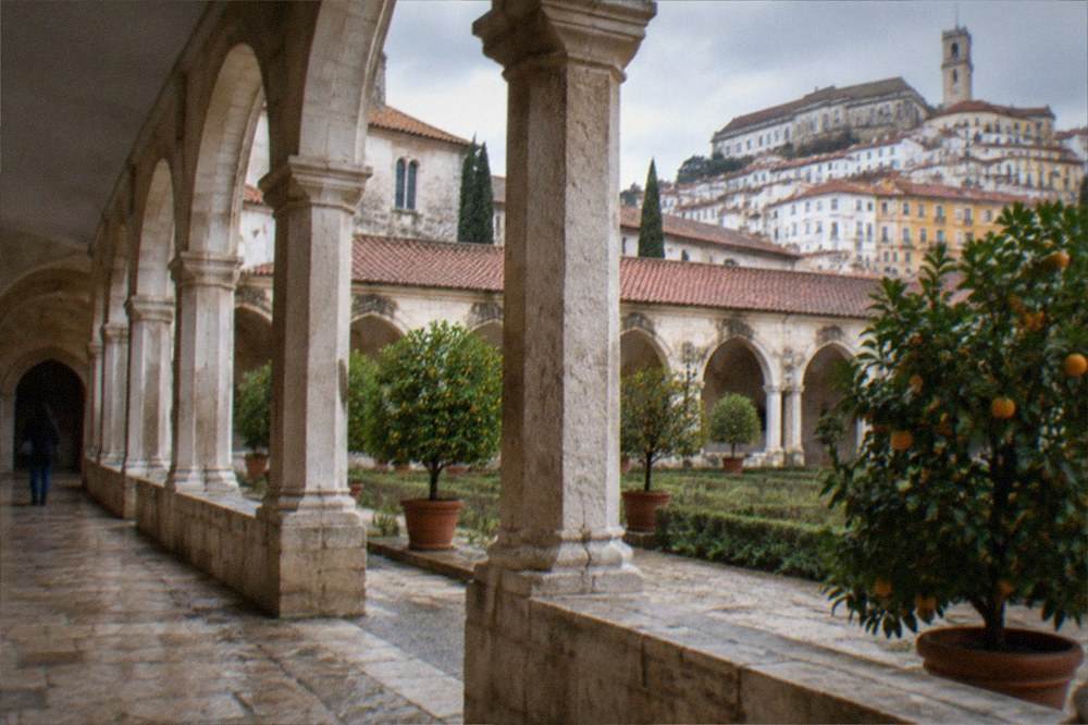 A quiet stone cloister walk with arches and potted orange trees at a Coimbra monastery