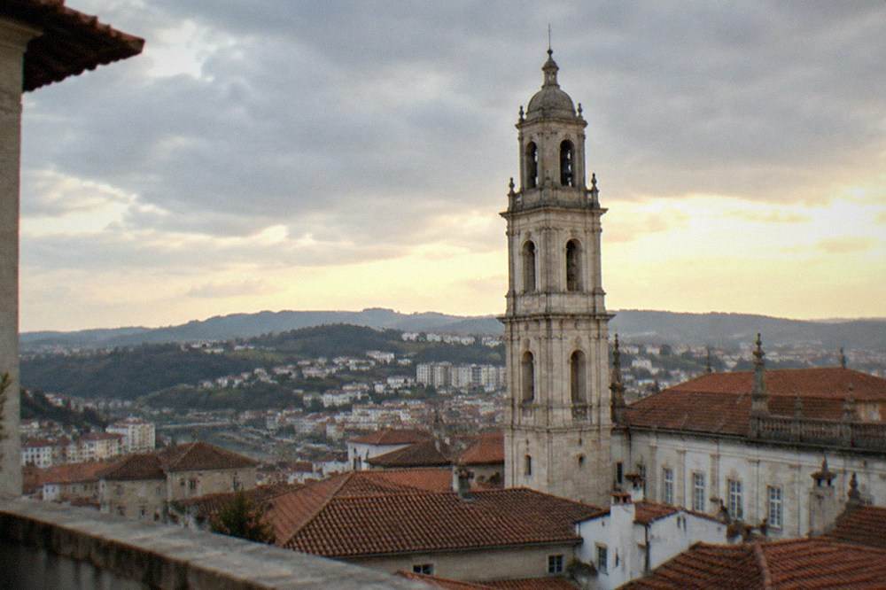 The baroque clock tower seen from a rooftop terrace across the old city at golden hour