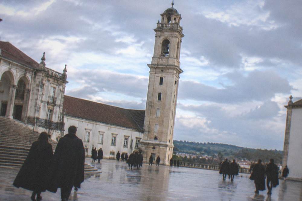 Students in black capes crossing the Paço das Escolas courtyard beneath the clock tower