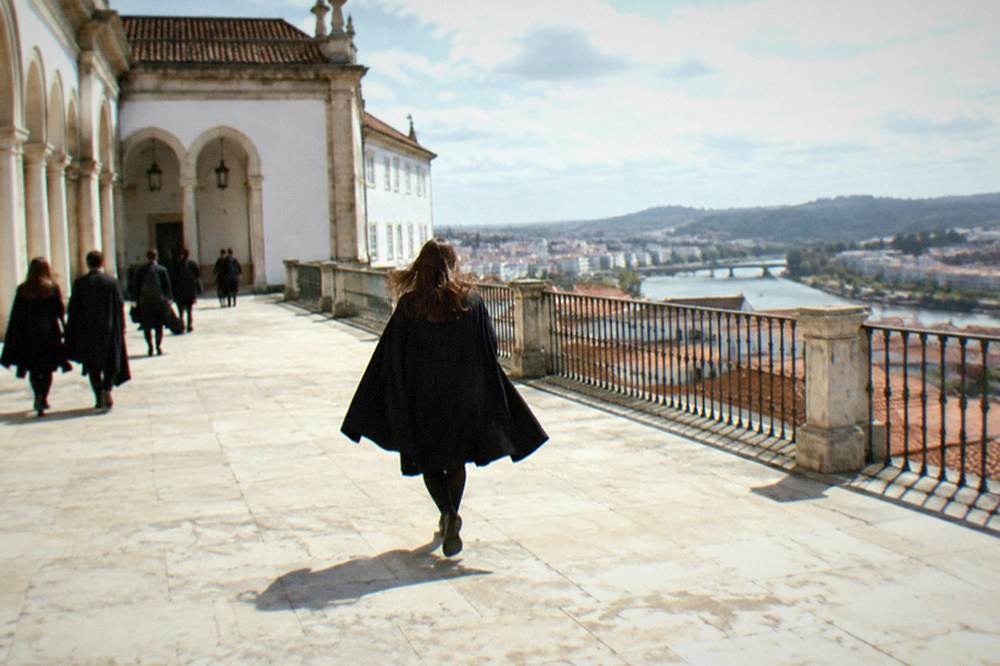 Students in black capes walking through the arcaded courtyard of the Paço das Escolas at the University of Coimbra