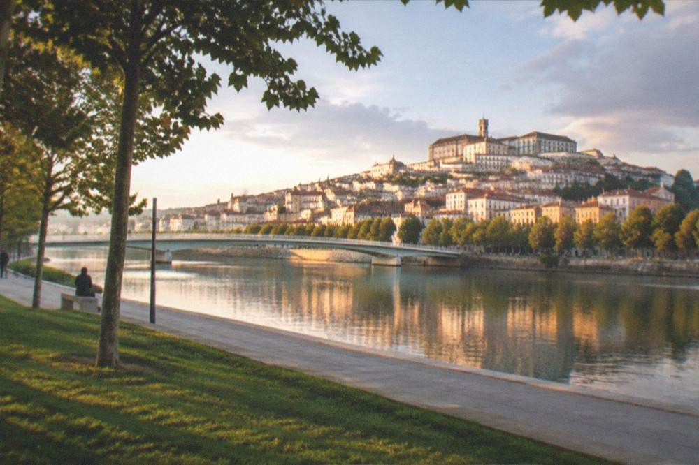 Evening view of the illuminated old town of Coimbra reflected in the River Mondego