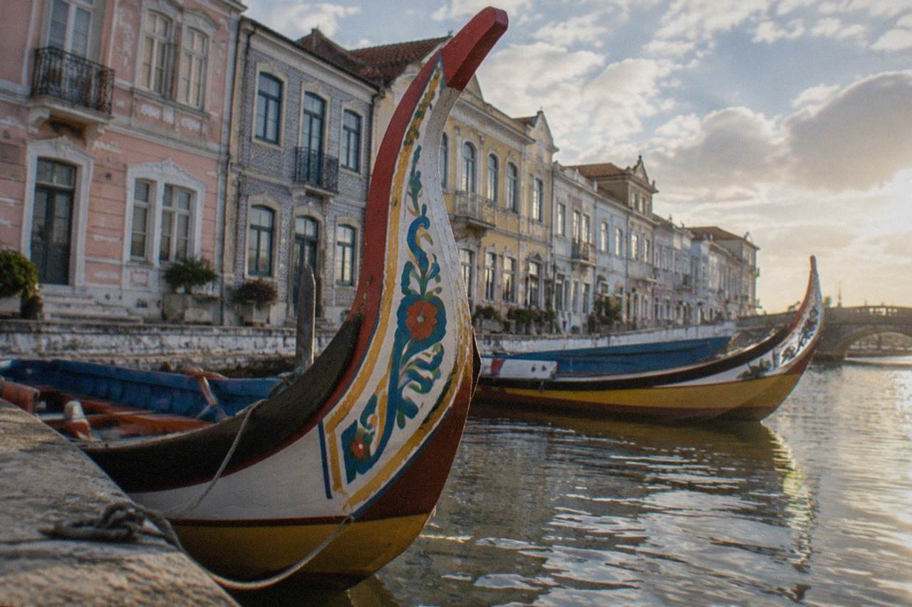 Colourful Aveiro canal boats moored beside pastel-fronted buildings on a sunny afternoon