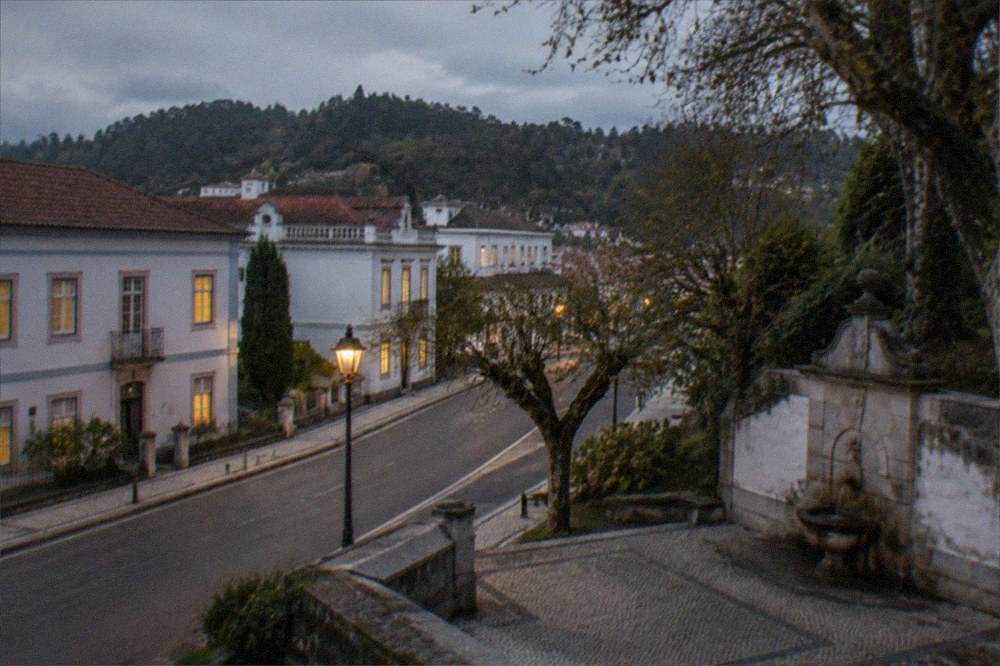 An evening view of a Portuguese spa town street with lit windows and empty sidewalks
