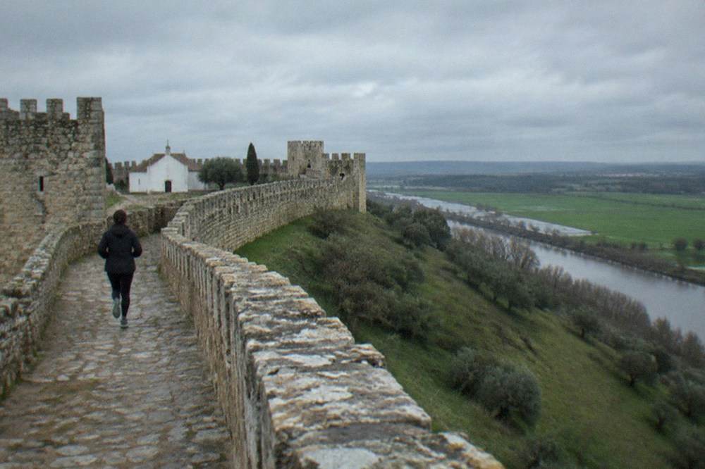 A crenellated stone wall walk curving along a hilltop with towers at intervals