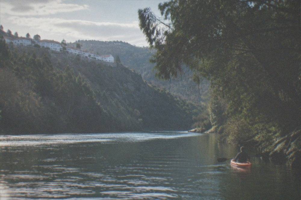 A single kayak close to a wooded riverbank, overhanging trees shading the water