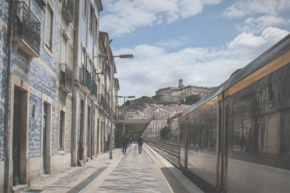 A regional train waiting at a small Portuguese station platform with a town visible beyond