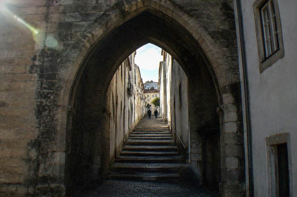 The stone archway of the Arco de Almedina framing a narrow ascending street in Coimbra's old town