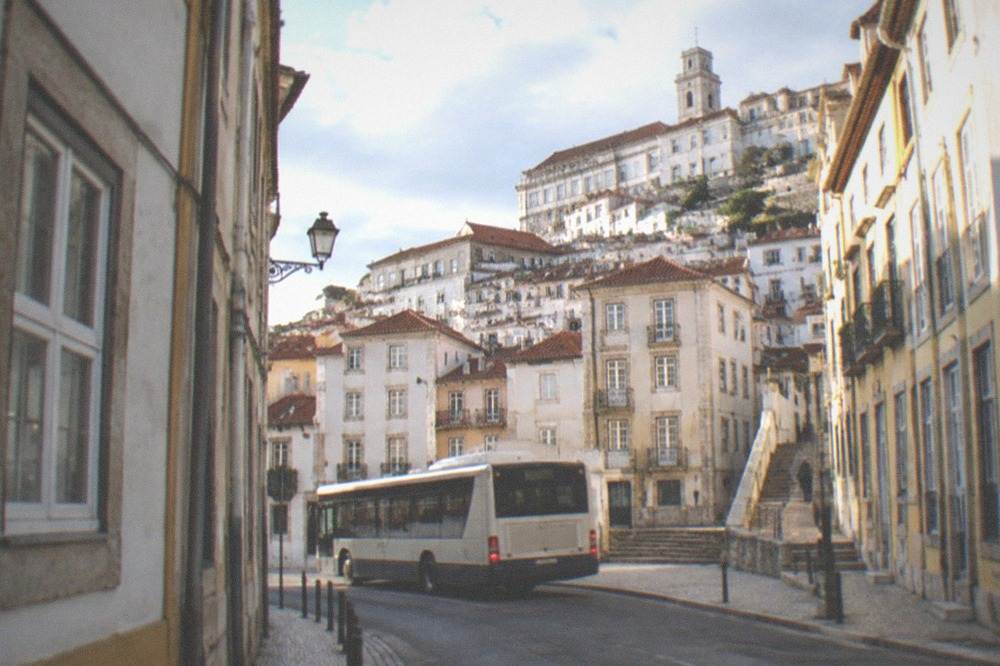 A city bus turning on a street in central Coimbra with the old town rising behind it