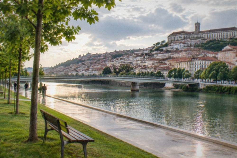A smooth riverside promenade beside the Mondego with the old university buildings visible high on the opposite hillside