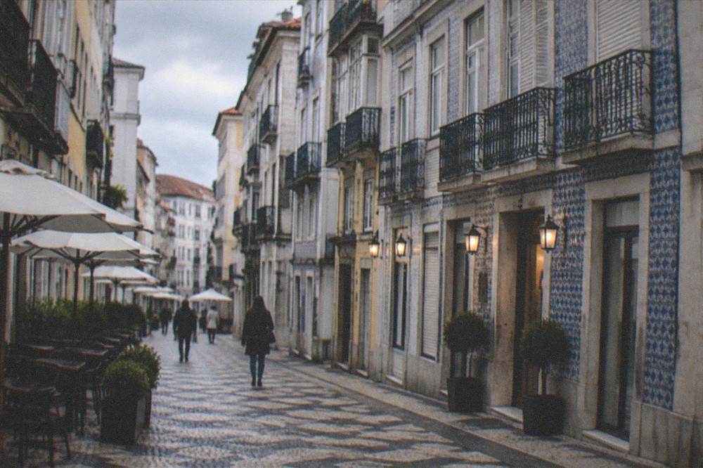 A quiet flat street in the Baixa downtown of Coimbra with hotel facades and cafe tables along the pavement