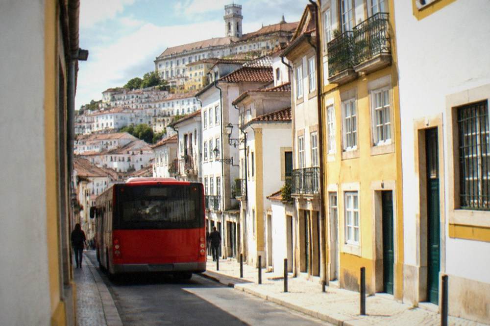 A red city bus stopped on a narrow street in central Coimbra