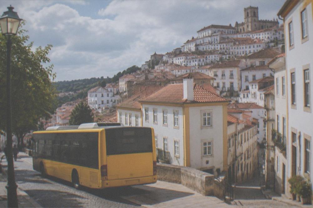 A yellow city bus stopped on a Coimbra street with the old town rising behind it
