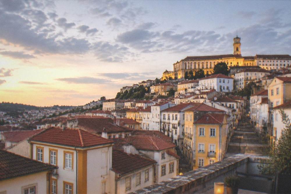 Evening view from a Coimbra rooftop terrace with the illuminated university buildings above the old town
