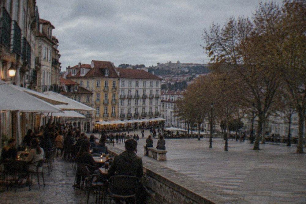 People sitting at outdoor tables on a narrow stone street in a Portuguese old town at dusk