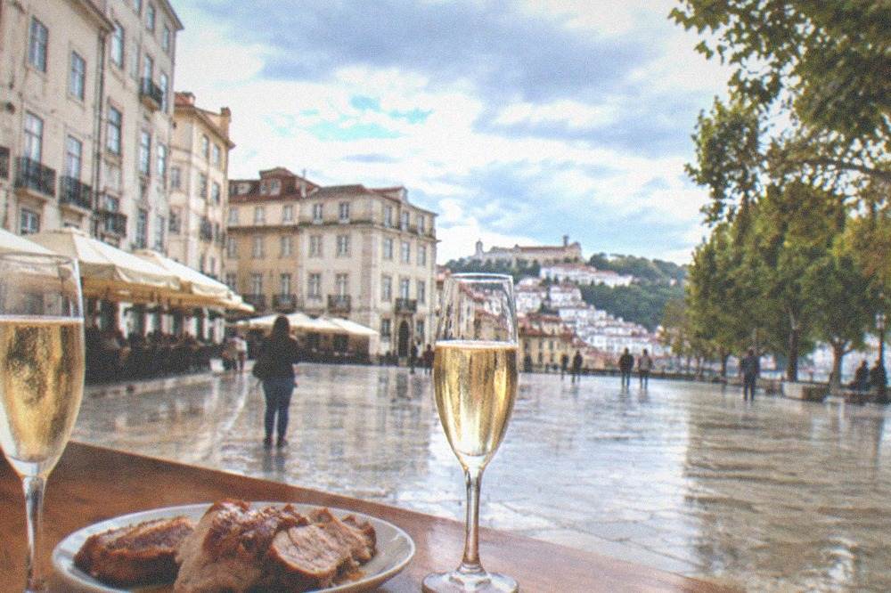 Two glasses of sparkling wine on a wooden bar counter beside a plate of sliced roast pork