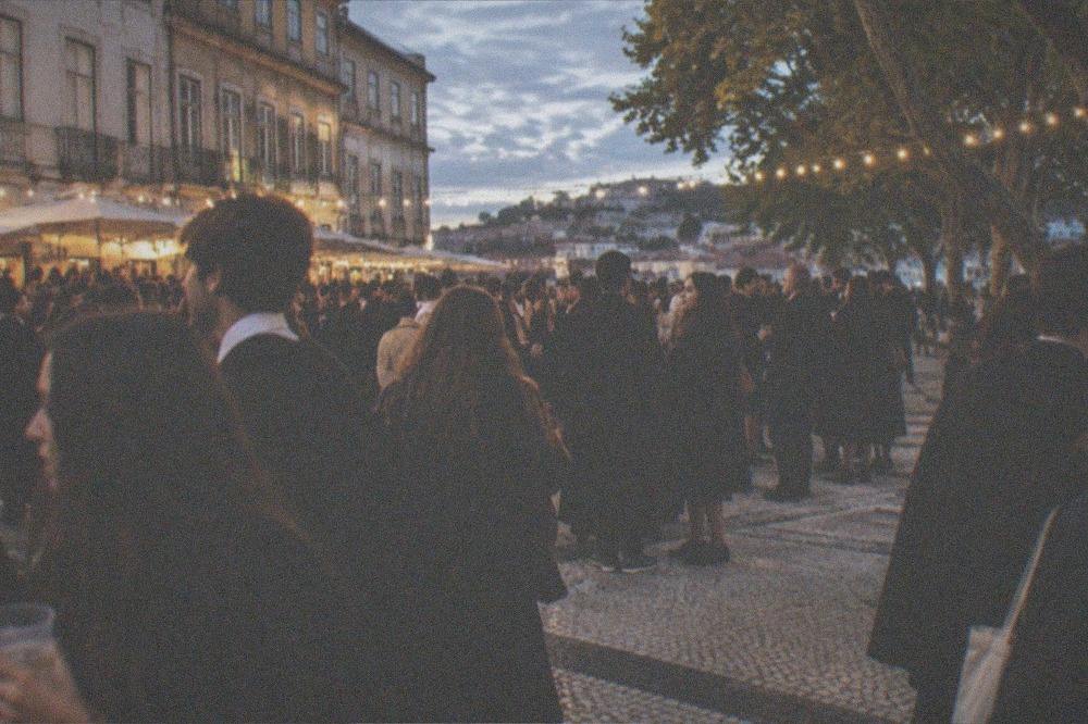 A crowded square at night with students in black capes celebrating under string lights