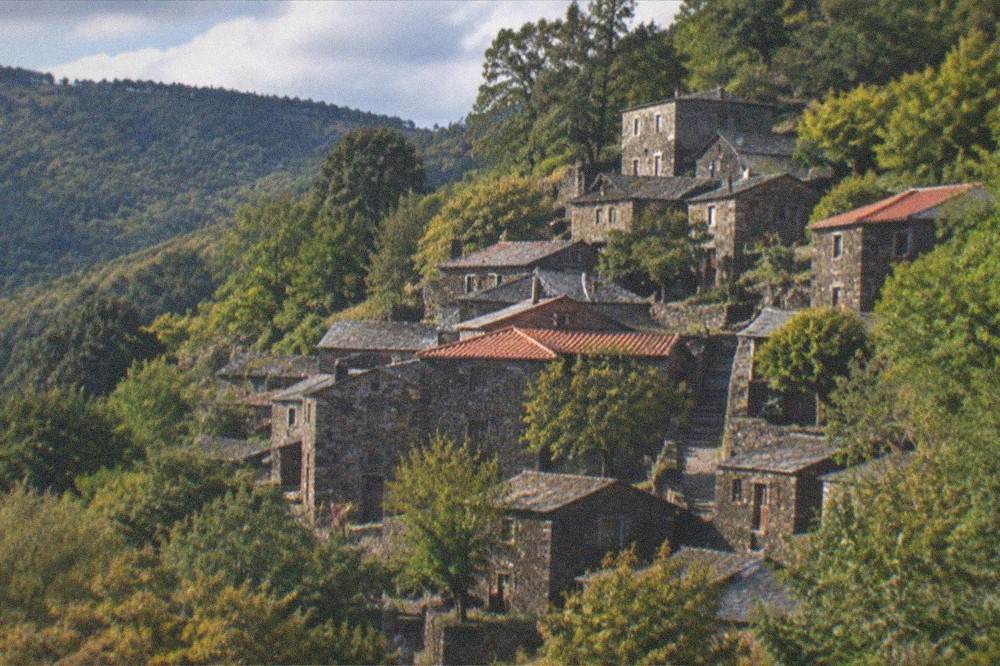 Stone schist village houses on a green mountainside in late afternoon light