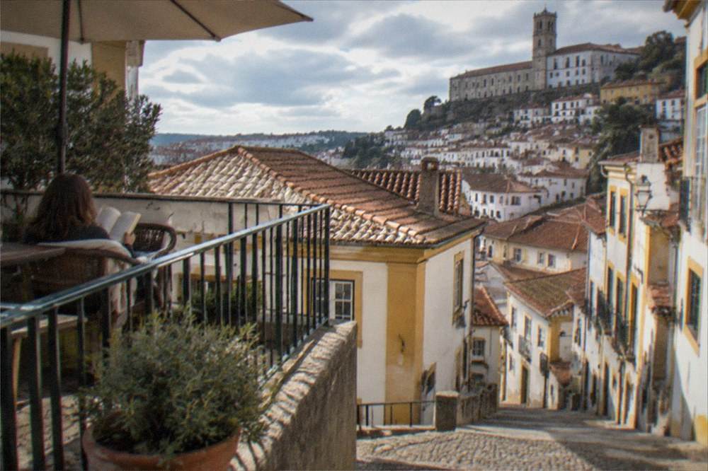 Guest reading on a shaded hotel patio above the tiled roofs of Coimbra