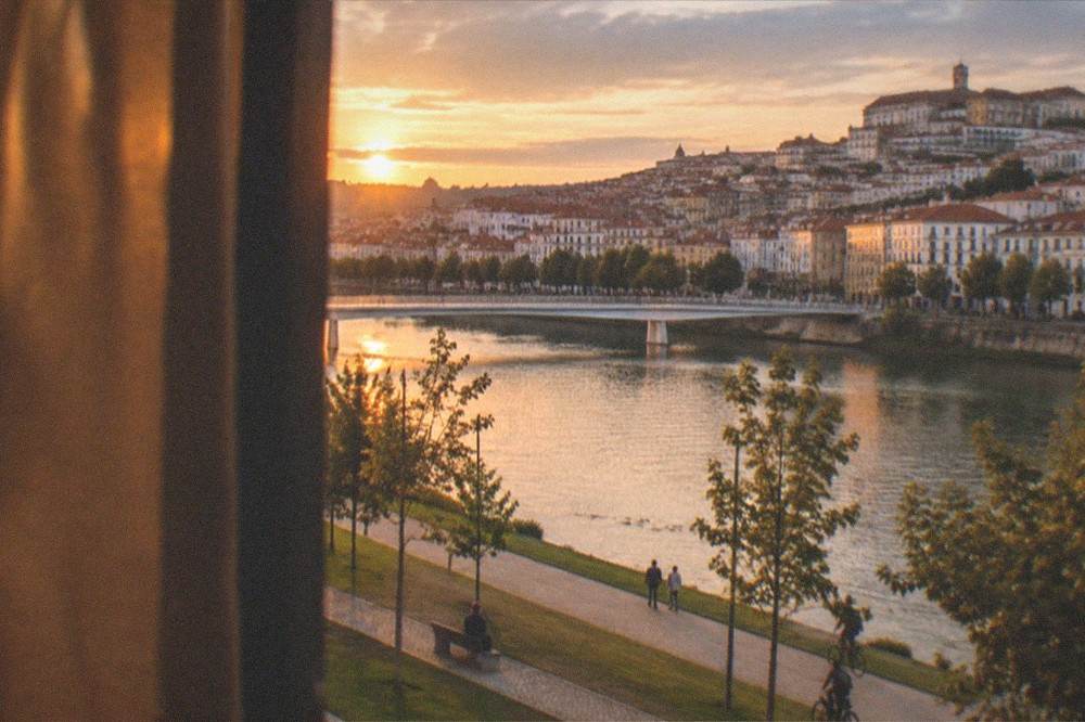 Evening view from a Coimbra hotel window with warm lights over the old town and the Mondego river