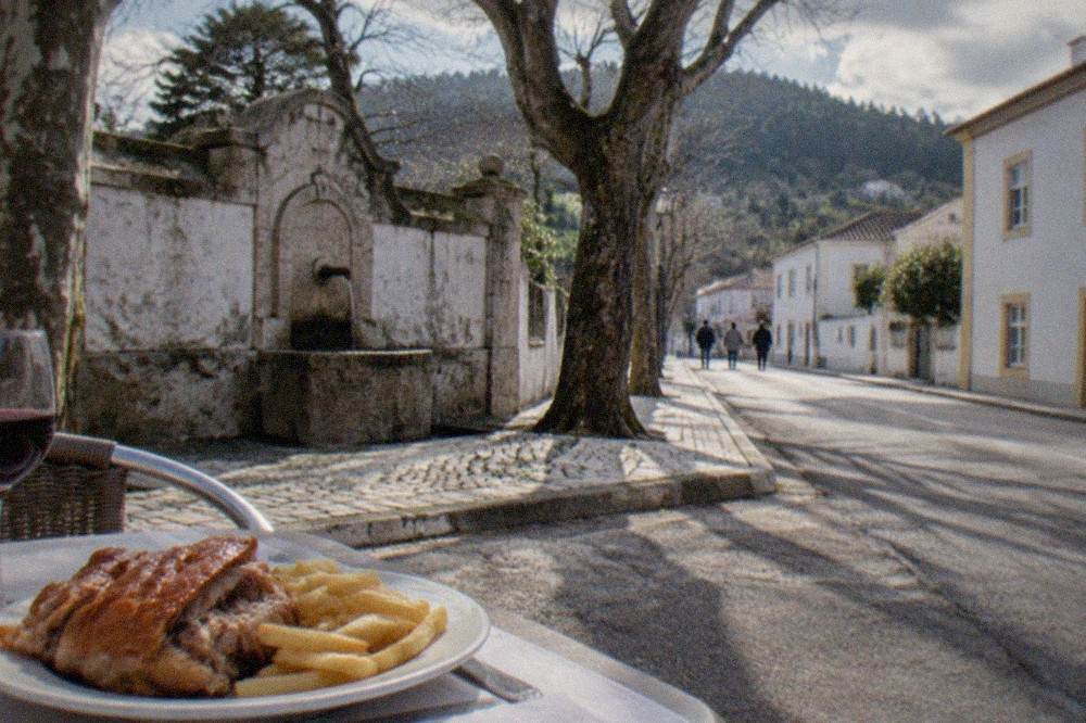 A plate of roast suckling pig with crisp skin, served with chips and a glass of red wine