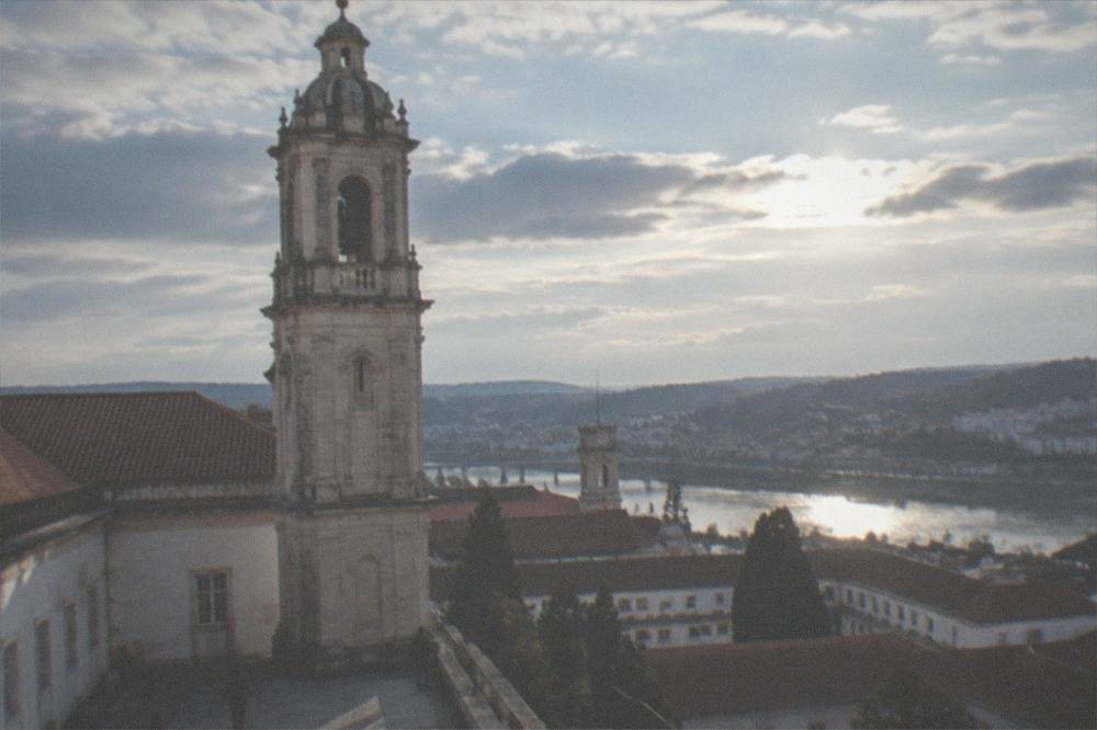 University courtyard with a clock tower above red rooftops and a river