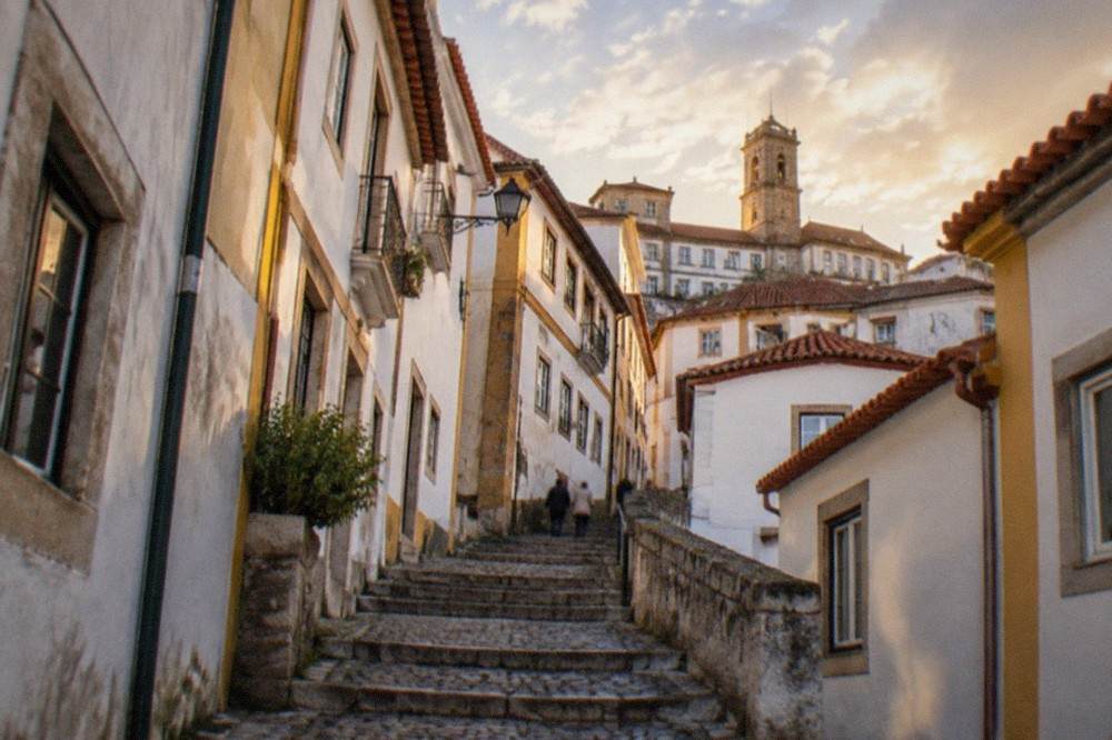 A narrow cobbled street in the old town of Coimbra with whitewashed walls and stone steps
