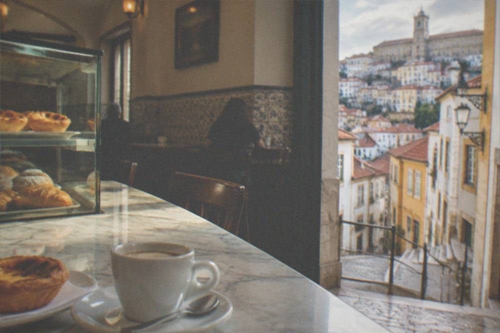 A small traditional Portuguese café interior with a marble counter and pastries in a glass case