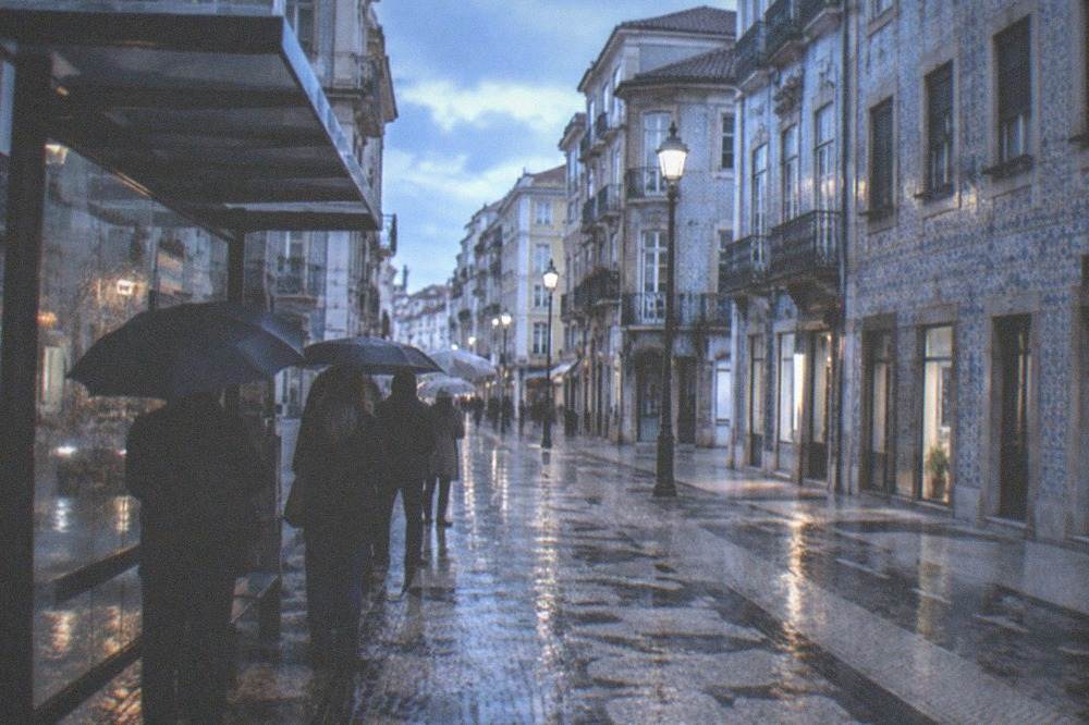 People waiting under a bus shelter while rain falls on a city street