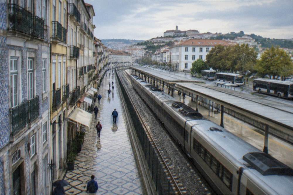 A railway platform with a passenger train alongside a view of buses on the street beyond