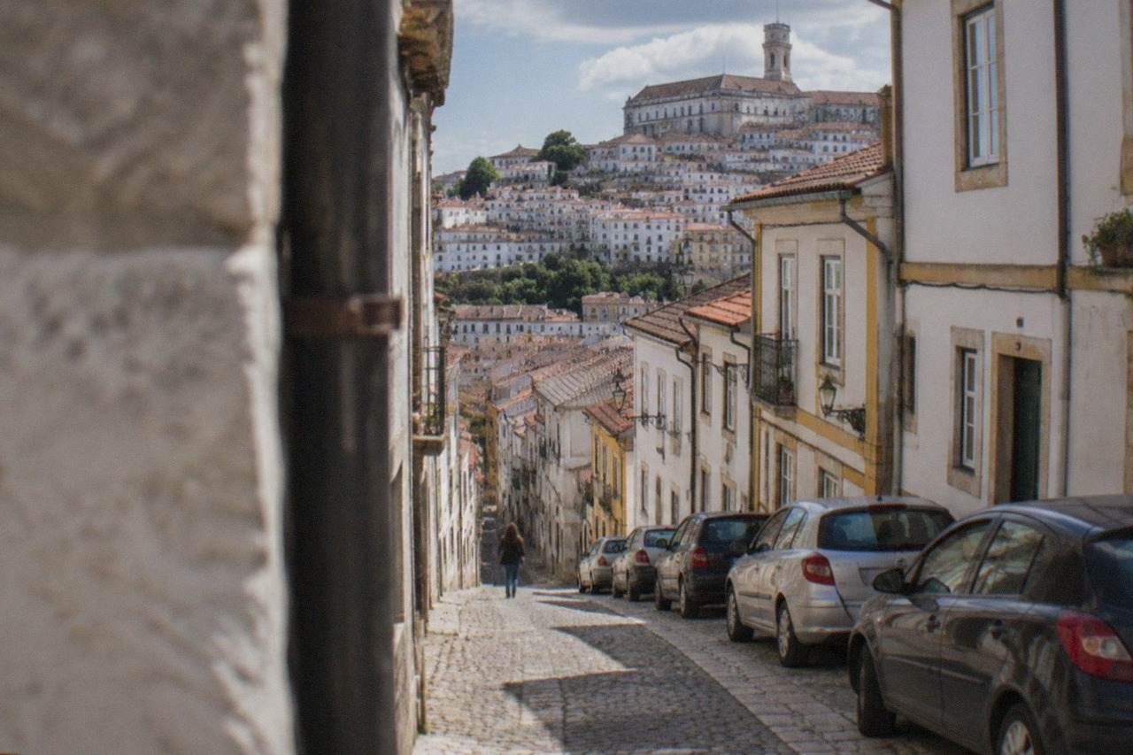 A narrow cobbled street in Coimbra's old town with parked cars squeezed against old stone buildings