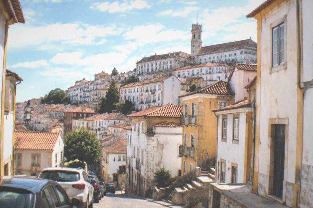 Cars parked along a sloped street with the tower of the University of Coimbra visible above rooftops