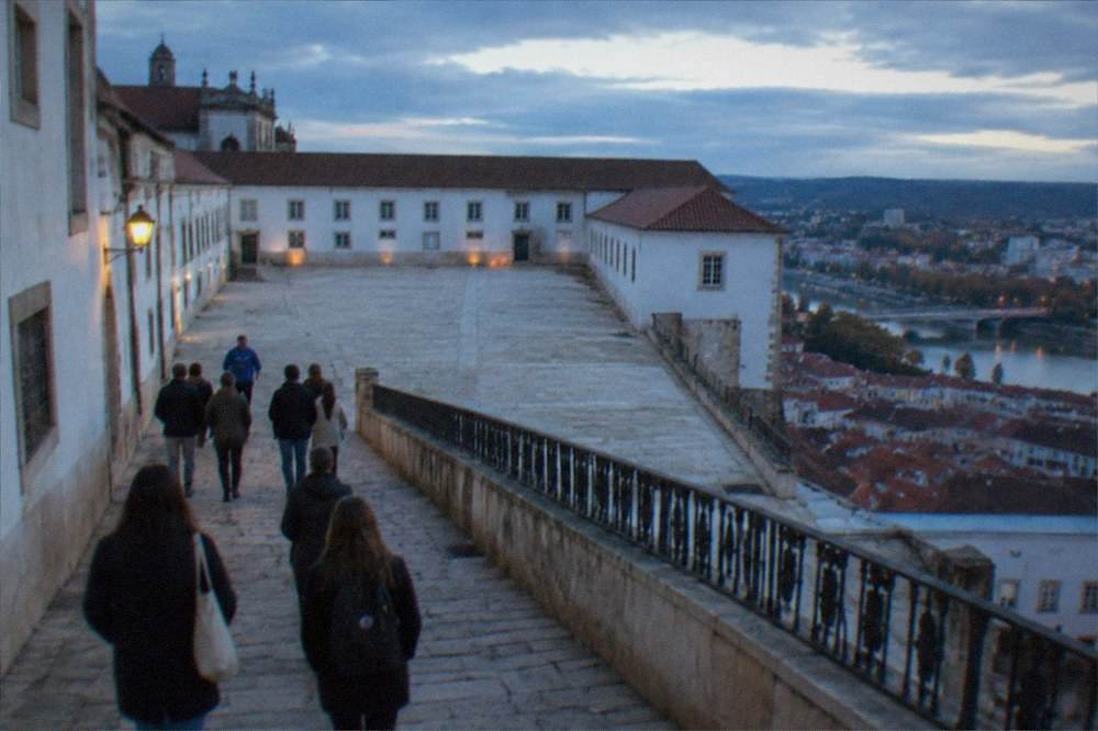 A group of walkers following a guide along a stone lane below the University of Coimbra buildings