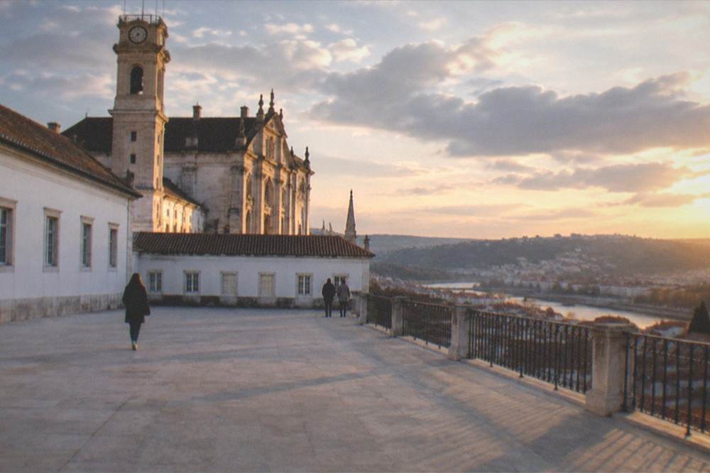 The baroque tower and facade of the University of Coimbra above the old town at golden hour