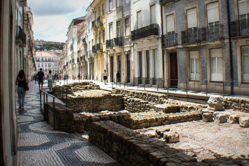 Visitors walking among the stone foundations of Roman house walls at an outdoor archaeological site