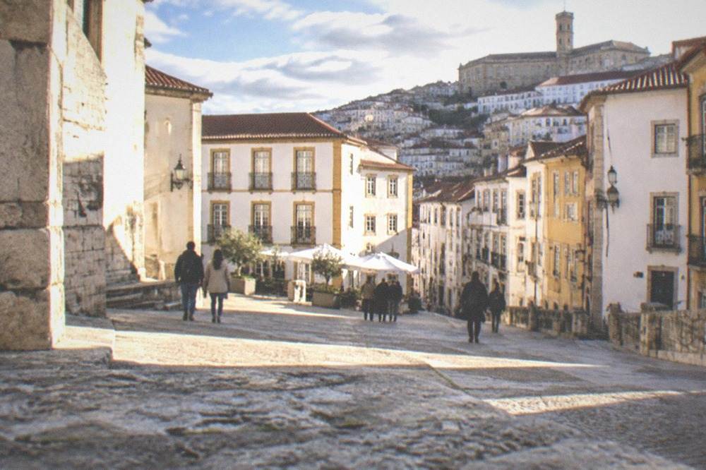 A sunny old-city square in Coimbra with people walking between stone buildings