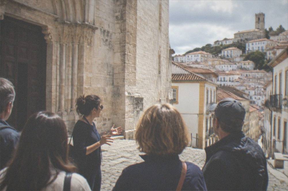 A guide speaking to a small group of visitors outside a church in Coimbra